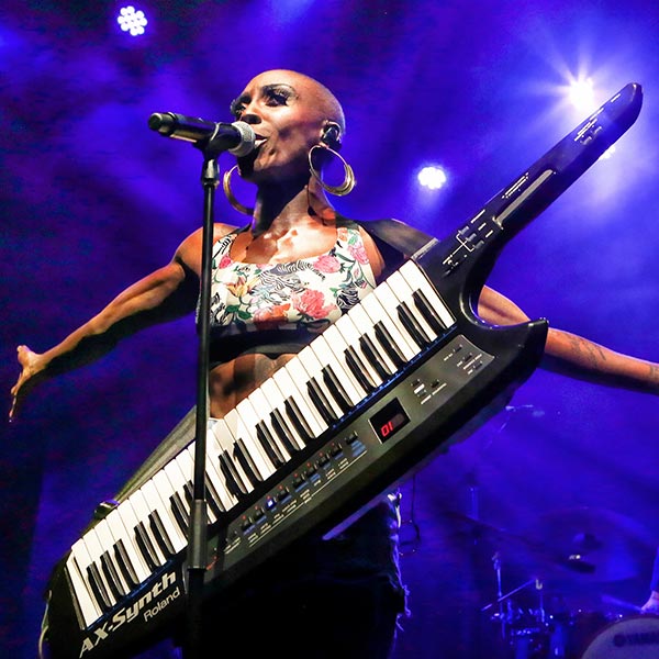 A performer singing into a mic stand and carrying a keytar.