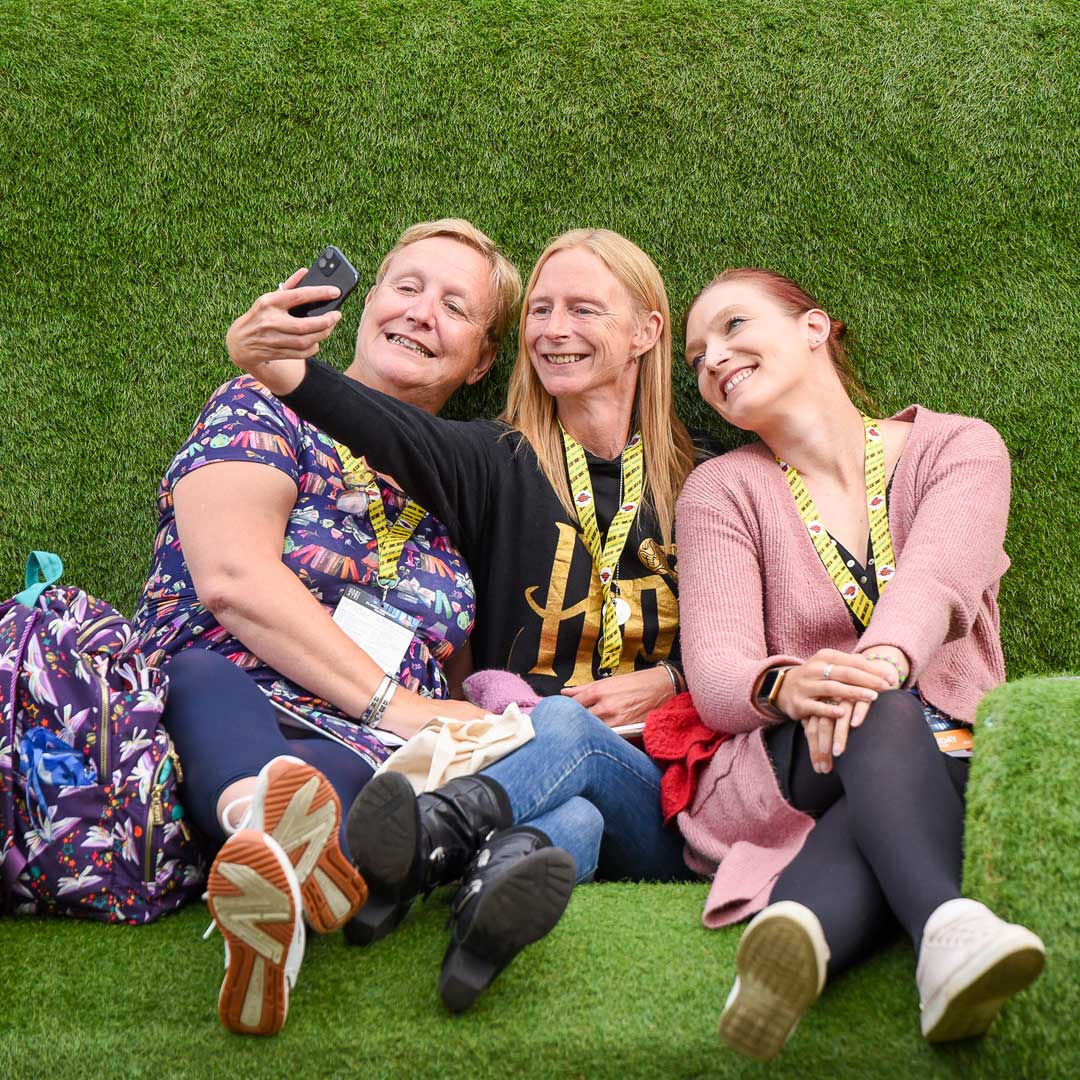 A group of three people taking a selfie sat outside on the grass furniture.