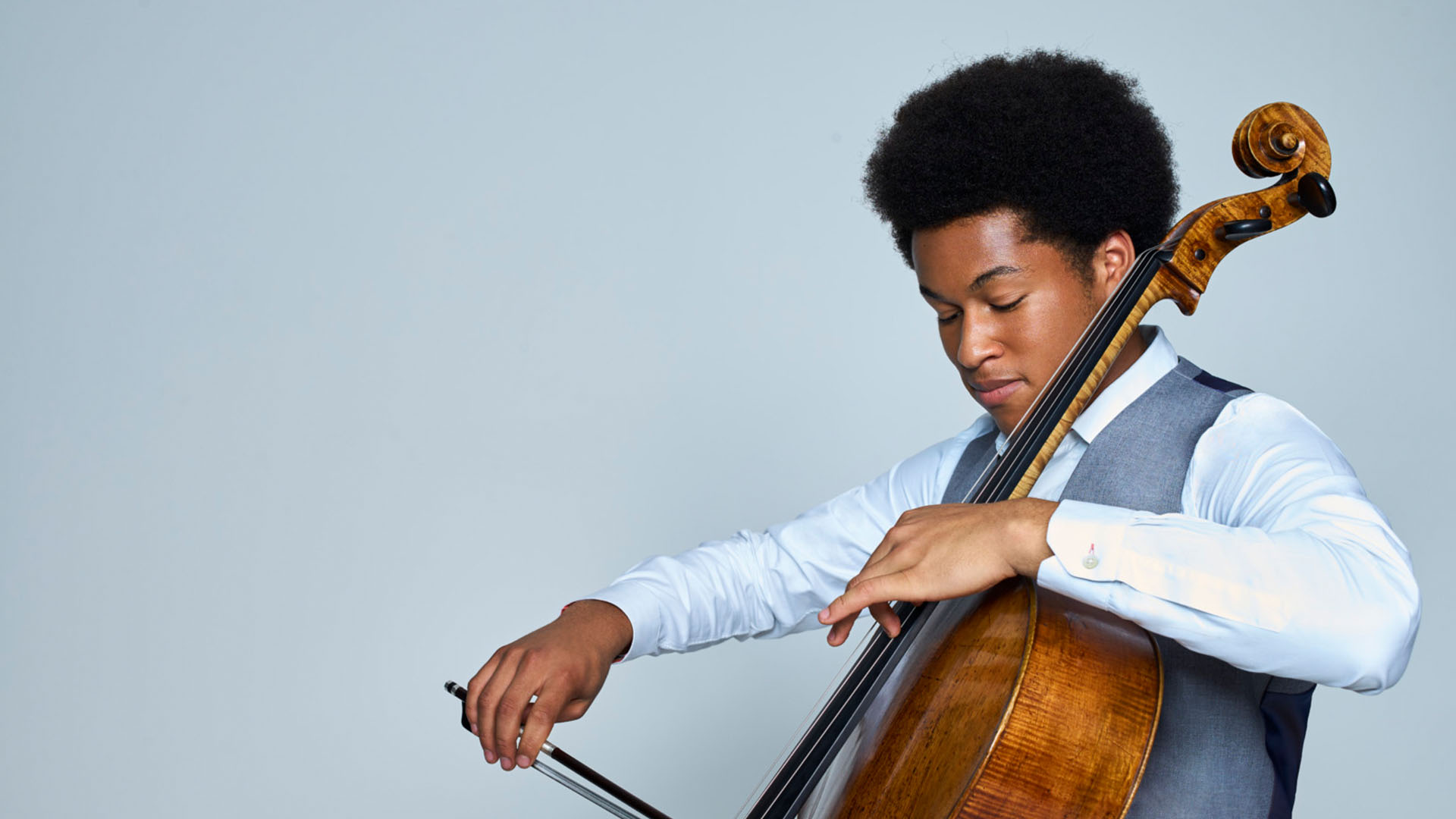 A person of colour playing the cello wearing formal wear.