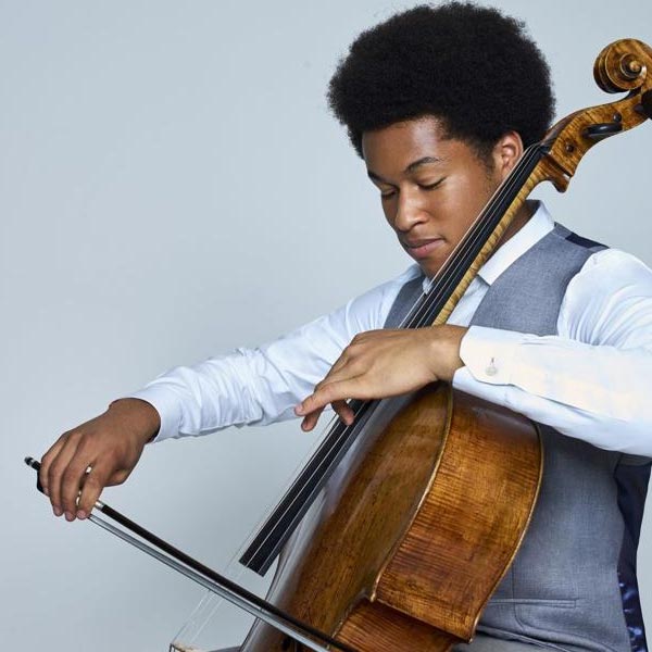 A person of colour playing the cello wearing formal wear.