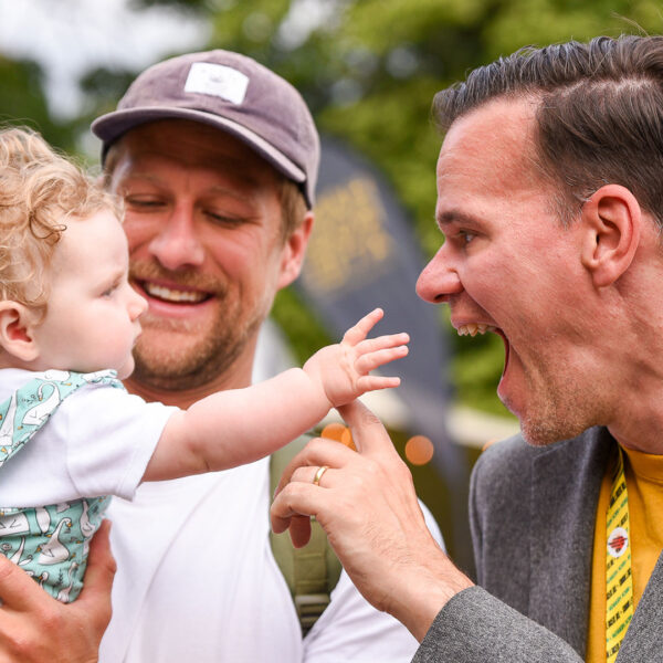 A man holding a baby stood next to another man who is smiling at the child.