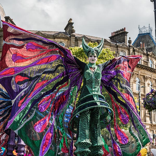 A street performer in a fantasty outfit with a horned helmet and colourful wings.