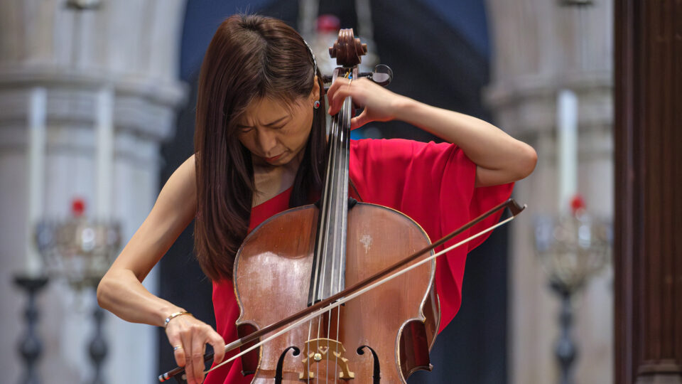 A woman wearing a red dress playing cello.