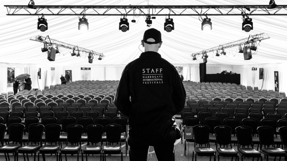 A HIF staff member stood on stage looking at the room full of empty seats. Above his head is a set of on stage lights.
