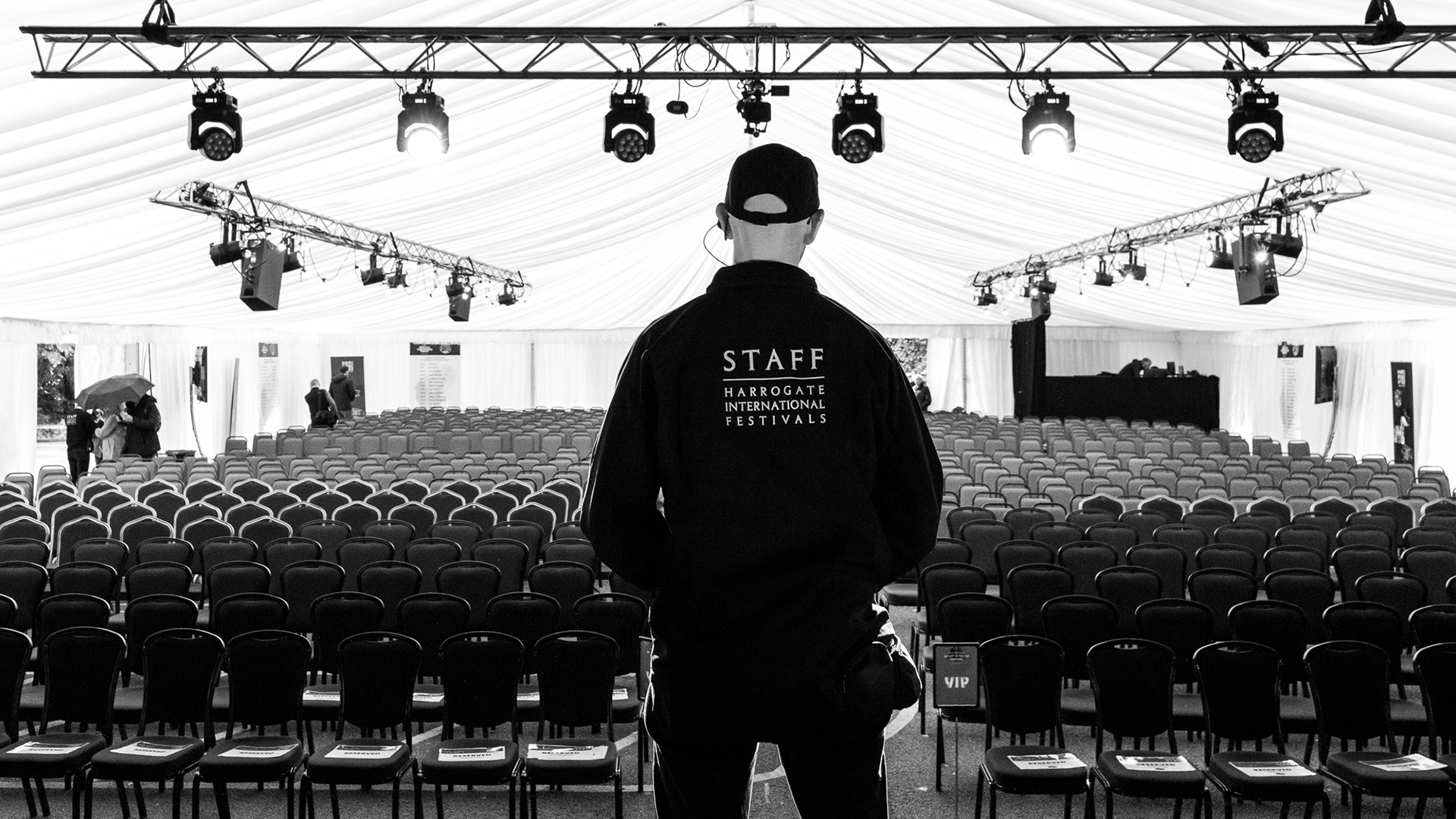 A HIF staff member stood on stage looking at the room full of empty seats. Above his head is a set of on stage lights.