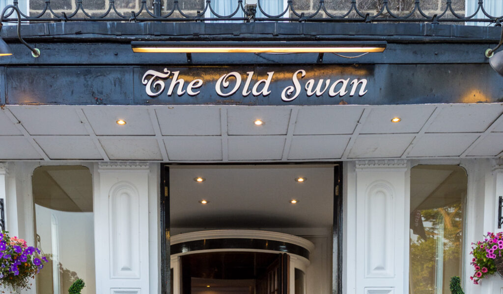 The outside of The Old Swan hotel showcasing the sign underneath an overhead light.