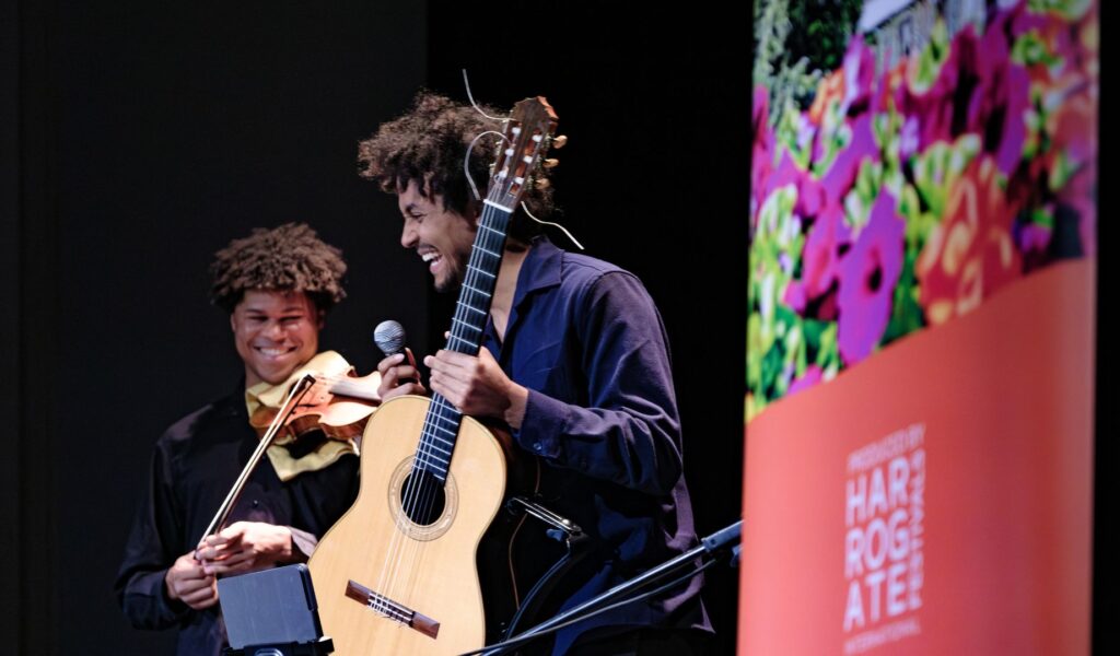 A violin player and acoustic guitar player on stage performing and smiling.