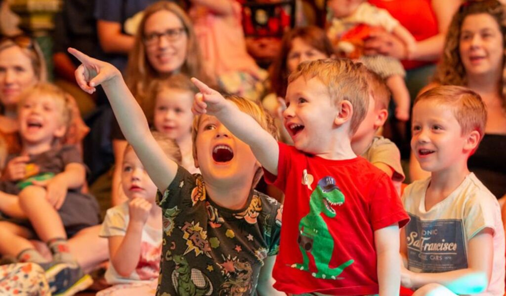Children in the audience at the childrens festival looking engaged, pointing and smiling.