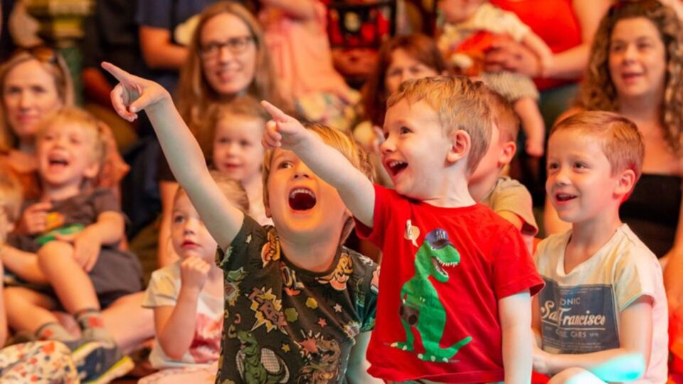 Children in the audience at the childrens festival looking engaged, pointing and smiling.