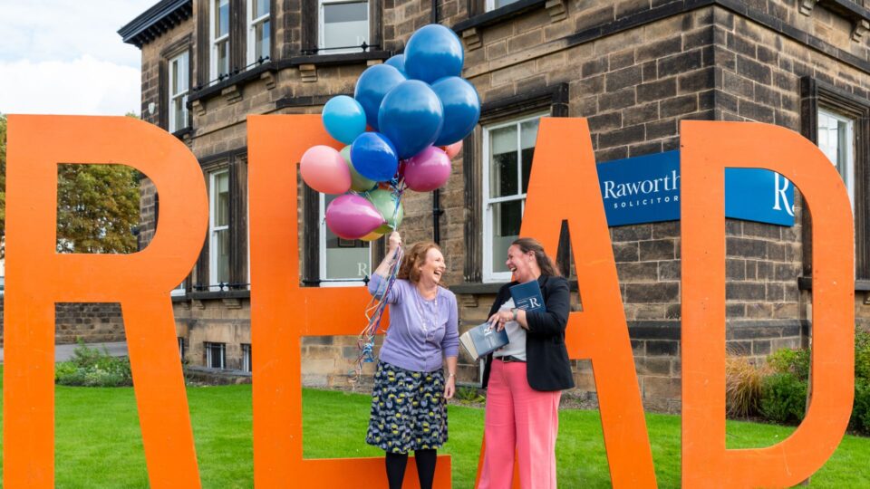 Sharon Canavar and Rachel Tunicliffe holding balloons and standing in front of the READ sign. They are outside the Raworths office.