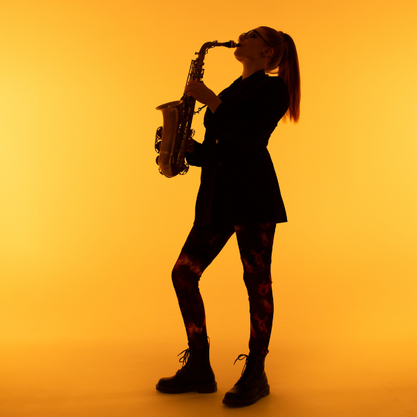 A silhouetted musician plays a saxophone against a bright orange background.