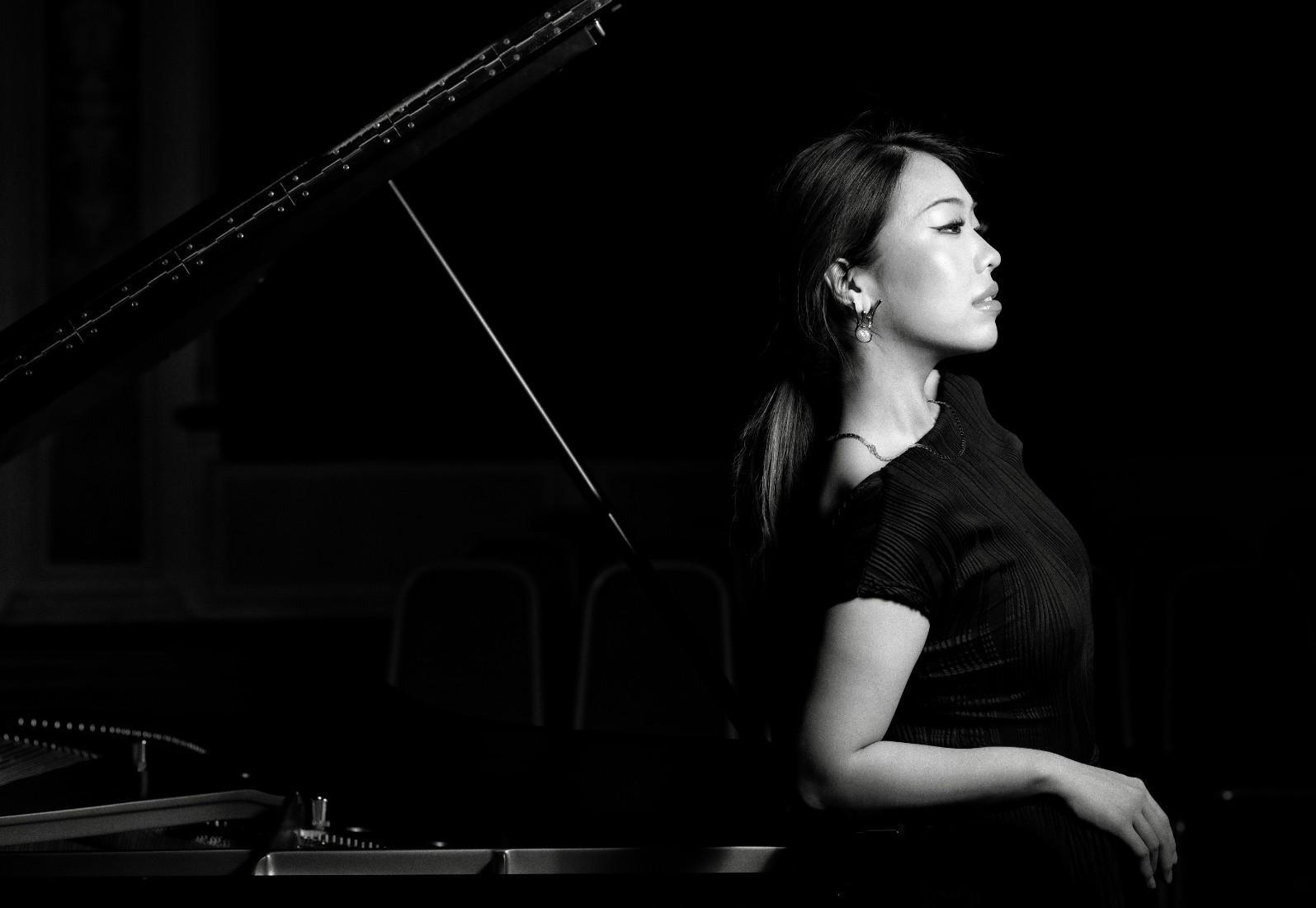 Black and white image of Junyan Chen stood beside her piano